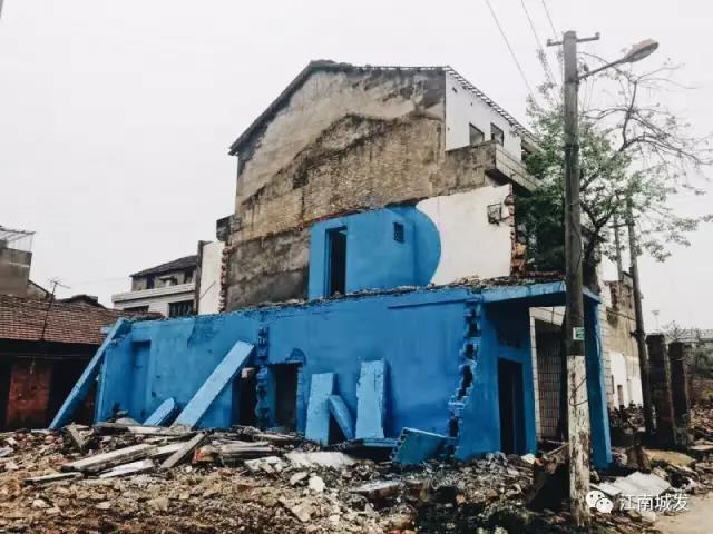 △ 這棟建筑是臨江最近的半拆遷建筑物的遺留，沅江和堤壩成為了展覽的天然背景。創(chuàng)作團(tuán)隊(duì)對(duì)這棟建筑進(jìn)行了半涂裝，將符號(hào)性的沅水曲線與拆遷進(jìn)行中的建筑立面進(jìn)行意義的疊造，它們共同觸發(fā)了場(chǎng)所空間多元語(yǔ)境的生成，把拆遷這種暫時(shí)破壞性、干擾性的介入行動(dòng)與沅水右岸發(fā)展的未來(lái)性、美好性緊密融合。